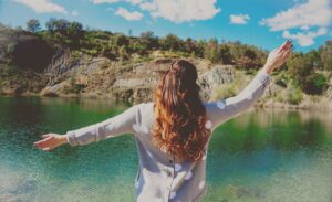 Lading standing with arms up in front of lake