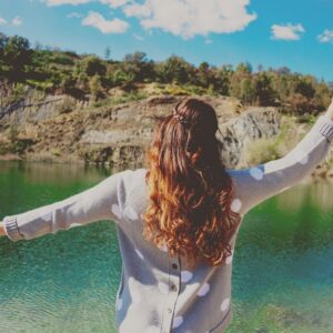 Lading standing with arms up in front of lake